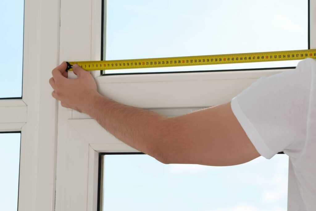 A professional window treatment installer with a yellow measuring tape measuring windows near Natick, Massachusetts (MA)